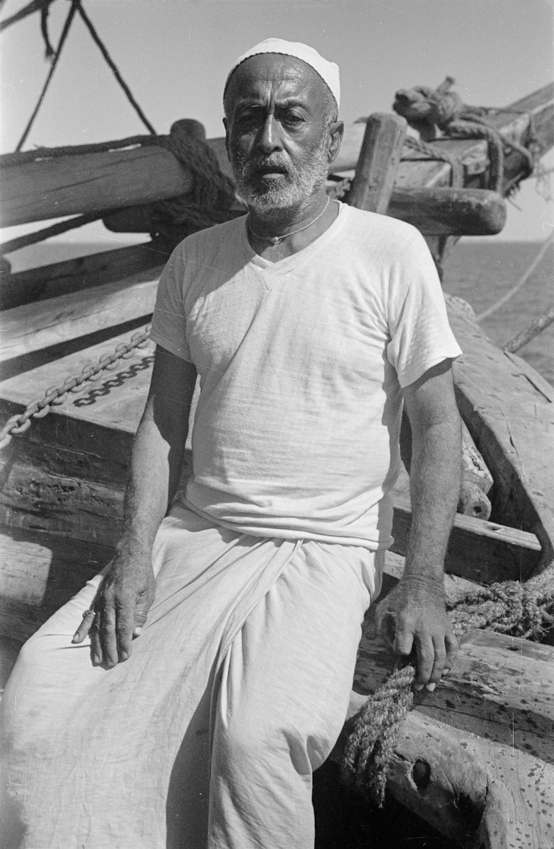 Three-quarter length seated portrait of Captain Haji Mansur on his dhow (sailboat) in the Persian Gulf near Bahrain.