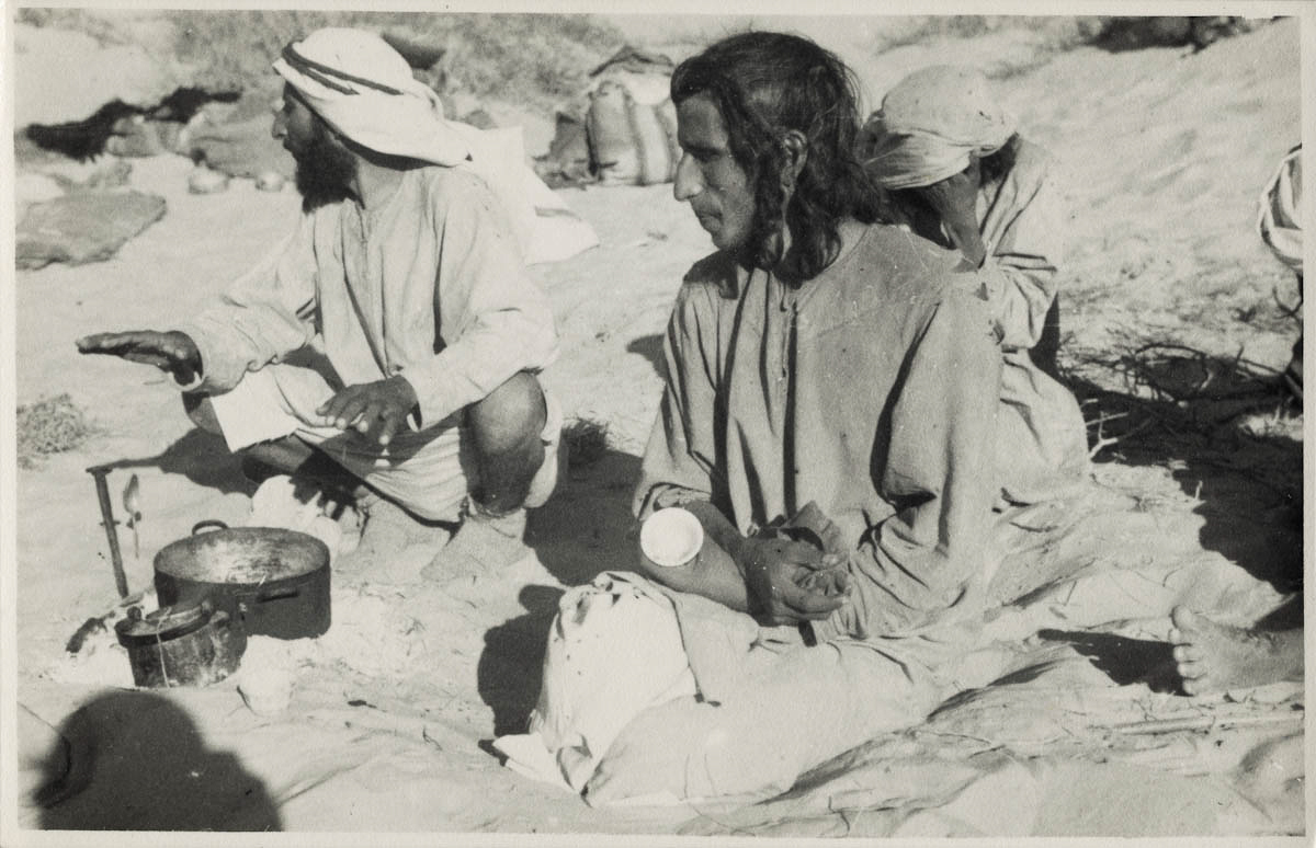 Portrait of Hamad bin Saadna and two Rashid tribesmen sitting beside a cooking fire at the encampment of Muhammad, a sheikh of the Rashid Bedouin, near Bir al Tawil in the Ramlat ar Rabbad.