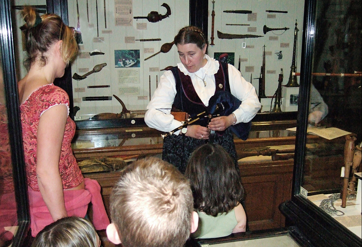 Hélène la Rue demonstrating the Northumbrian pipes to a group of children in the Pitt Rivers Museum [1998.356.23.6]