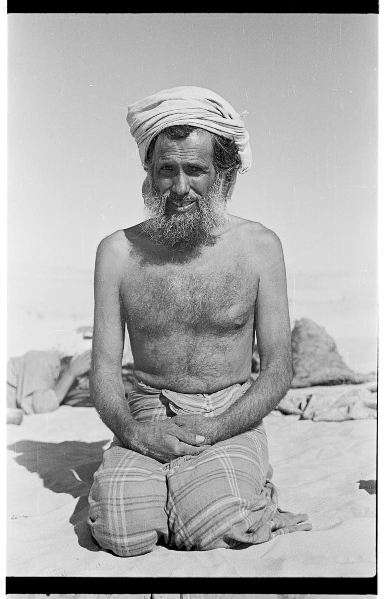 Seated portrait of Sahail bin Tahi, a tribesman of the Mudairiba lineage of Rashid Bedouin and one of Wilfred Thesiger's guides, during the party's journey from Al Ain to Liwa oasis (likely in the region of Al Humrah sands).
